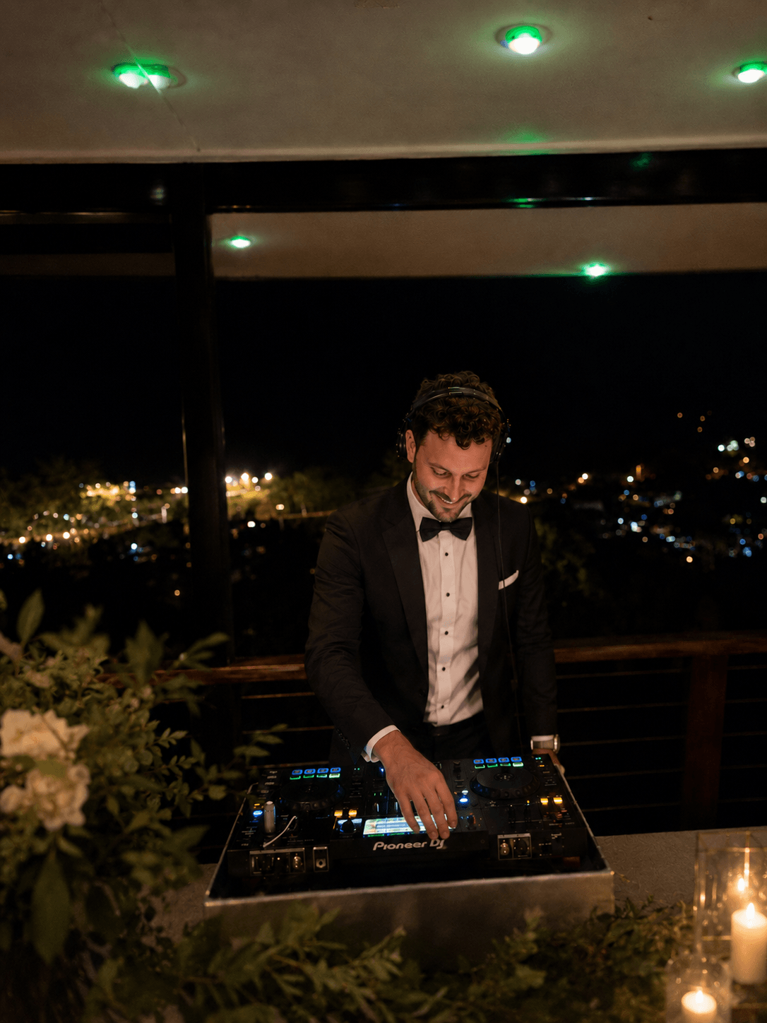 JANORIS in a tuxedo behind the decks at a wedding under string lights